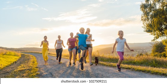 Playful Family Running And Playing On A Path In Backlit Summer Landscape