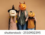 Playful family wearing costumes posing and having fun, holding carved pumpkin isolated on beige background, halloween celebration concept