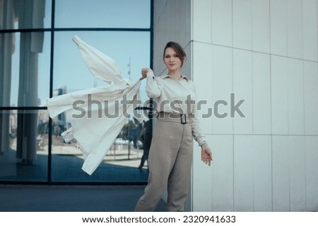 Playful fashion business woman in stylish beige pant suit standing near office building and confidently look at camera, copy space.