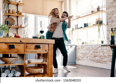 Playful. Full length of beautiful young couple in casual clothing dancing and smiling while standing in the kitchen at home           