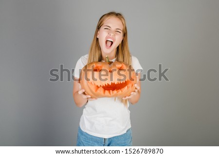 playful funny blonde girl with halloween jack o lantern pumpkin isolated over grey