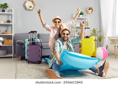 Playful funny couple having fun on air mattress at home, imagining themselves on summer vacation. Man and woman in summer hats and sunglasses are having fun at home among colorful suitcases. - Powered by Shutterstock