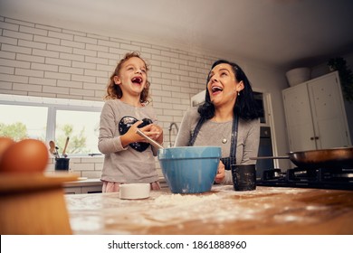 Playful Girl Laughing With Mother In Kitchen While Preparing Dough On Messy Worktop