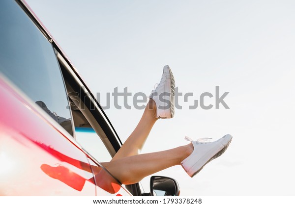 Playful girl\
sticking out feet in white sneakers from vehicle at sky background,\
happy traveling\
adventure.