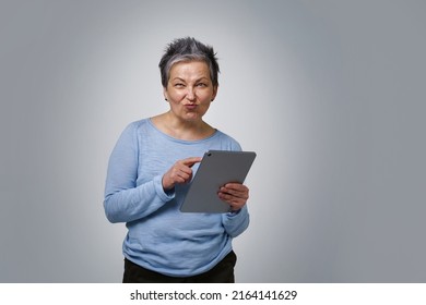 Playful grey haired mature woman with digital tablet working or checking on social media. Pretty woman in 50s in blue blouse isolated on white background. Older people and technologies.