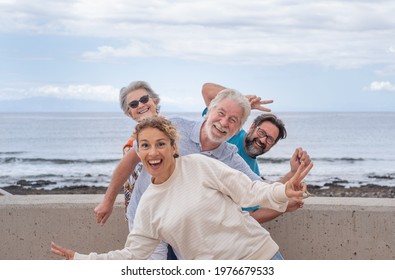 Playful group of multigeneration family looking at camera joking outdoor by the sea. Horizon over water and cloudy sky - Powered by Shutterstock