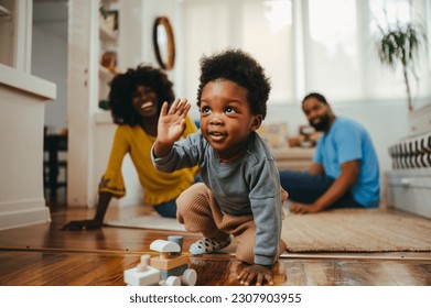 A playful happy african american child is playing a game with a Montessori train toy while his parents are laughing at him from the background. A happy child is having fun while learning from home. - Powered by Shutterstock