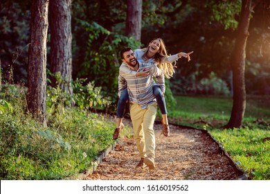 Playful happy handsome caucasian couple having piggyback while walking on trail in woods. Adventure in nature concept,
