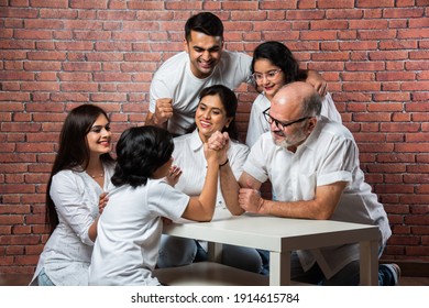 Playful Indian Asian Kid And Grandfather Arm Wrestling At Home With Other Family Members Looking, Wearing White Cloths