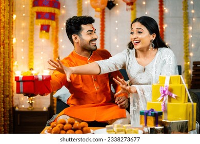 Playful Indian brother playing with sister by not giving gift box during raksha bandhan festival - concept of festival celebration, relationship bonding and togetherness.