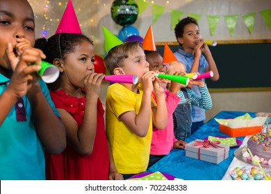 Playful Kids Blowing Party Horns While Standing By Table