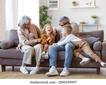 Playful kids and grandmother with grandfather tickling each other  while having fun at home, happy family senior grandparents and children having fun together and playing while relaxing resting on sof