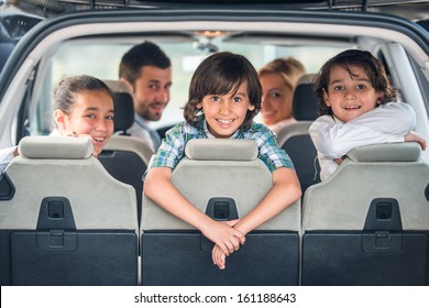 Playful Kids Posing In The Back Of A Car With Their Parents In Background