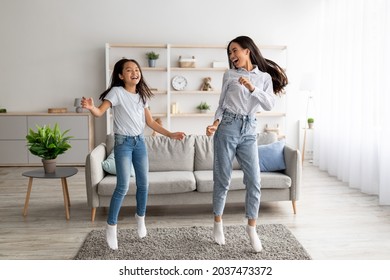 Playful Korean Mother And Pretty Daughter Dancing To Music And Jumping At Home. Asian Mom And Her Kid Enjoying Favorite Song Together, Fooling Around, Having Fun In Living Room Interior