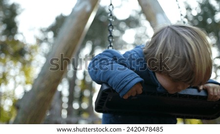 Playful Little Boy Twisting and turning while leaning on Park Swing during autumn fall park season. Carefree child engaged in play