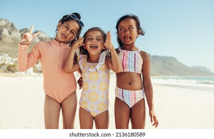 Playful little girls making funny faces while standing together at the beach. Group of adorable young friends having fun together during summer vacation. - Powered by Shutterstock