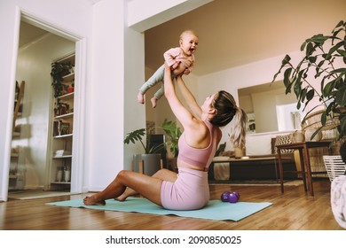 Playful mom lifting her adorable baby into the air. Happy mom working out with her baby on an exercise mat at home. New mom bonding with her baby during her post-natal fitness routine.