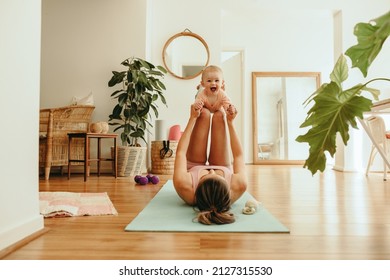 Playful Mom Lifting Her Adorable Baby With Her Legs. Yogi Mom Working Out With Her Baby On An Exercise Mat. New Mom Bonding With The Baby During Her Post-natal Fitness Routine.