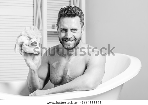 playful mood. macho enjoy bath. Sexy man in\
bathroom. Sex and relaxation concept. man wash muscular body with\
foam sponge. Wash off foam with water carefully. Macho naked in\
bathtub. funny\
duckling.