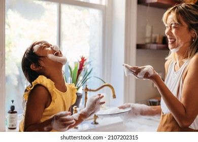 Playful mother and daughter having fun with soap foam in the kitchen. Happy little girl laughing cheerfully with soap bubbles on her face. Mother and daughter spending quality time together. - Powered by Shutterstock