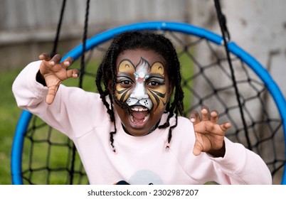 A playful outdoor portrait of a 6-year-old African American girl of Ethiopian descent, with her face painted like a lion. With a silly expression on her face, she exudes joy and creativity. - Powered by Shutterstock