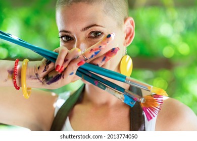 Playful portrait young gorgeous female painter artist  and hands covered in paint  looking   smiling at camera through her fingers  Creativity   individuality concept 
