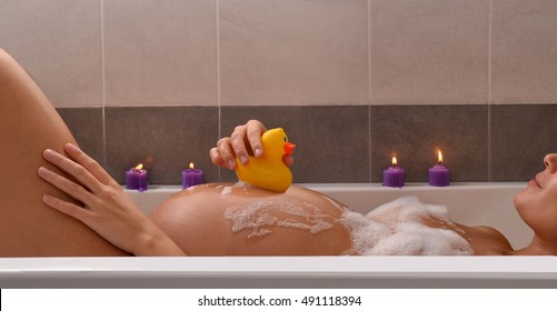 Playful pregnant woman in bathtub with rubber duck.Serene pregnant woman in relaxing candle ambient at bathtub before give Birth. Beautiful young pregnant woman at beauty salon spa.