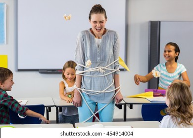 Playful schoolchildren tied up female teacher with rope in classroom - Powered by Shutterstock