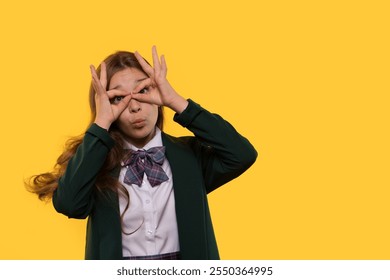 A playful schoolgirl making binoculars with her hands while posing. - Powered by Shutterstock