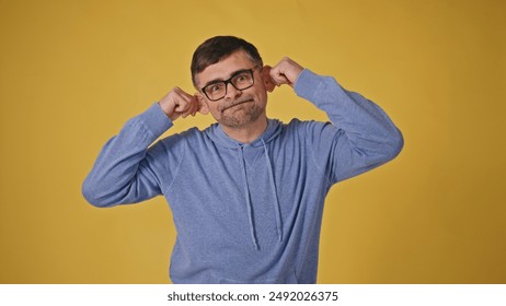 Playful senior man in glasses making monkey faces on yellow background - Powered by Shutterstock