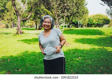 Playful Senior Woman Shows Off Her Tummy And Uses Her Hands To Hold Onto Excess Cellulite During Morning Outdoor Exercises In The Garden To Lose Weight Because She Wants To Stay Healthy.