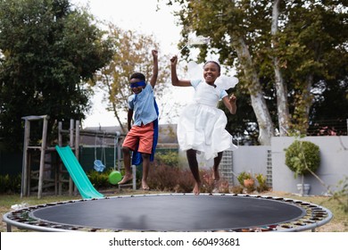 Playful siblings in costumes enjoying on trampoline at lawn - Powered by Shutterstock