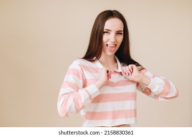 Playful, Spoiled Facial Expression, Sticking Out The Tongue, Showing Off On A Plain Beige Background. The Concept Of An Unbalanced Person.