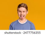 Playful teen boy winking and sticking out tongue, orange studio background
