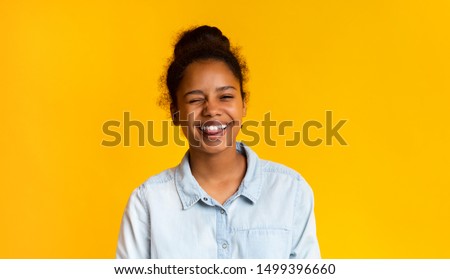 Playful teen girl winking and sticking out tongue on yellow studio background, copy space
