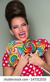 Playful Vivacious Woman With A Retro Beehive Hairdo Wearing A Red And White Polka Dot Dress Laughing As She Holds A Handful Of Colourful Spiral Candy Lollipops