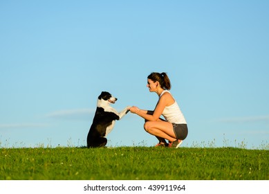 Playful woman and cute dog having fun and enjoying leisure outdoor. Sporty girl training her pet and playing around.