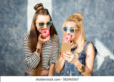 Playful women having fun with sweet donuts on the blue wall background