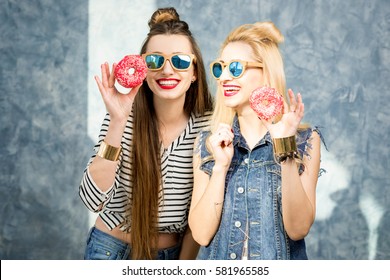 Playful women having fun with sweet donuts on the blue wall background