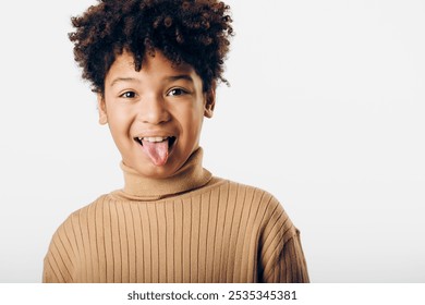 A playful young african american boy sticking out his tongue against a simple white background, radiating joy and mischief - Powered by Shutterstock