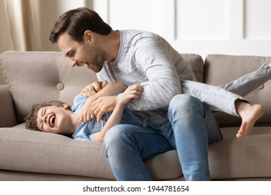 Playful young Caucasian father play with excited smiling small 8s son in living room at home. Overjoyed dad have fun with little preschooler boy child, tickle giggle, enjoy family weekend together.