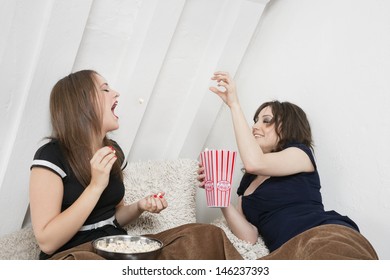 Playful Young Female Tossing Popcorn Into Friend's Mouth In Bed