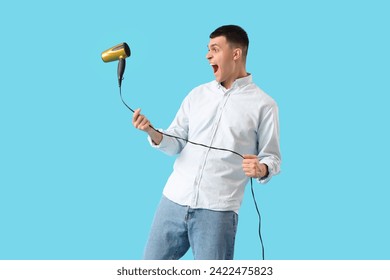 Playful young man with hair dryer on blue background