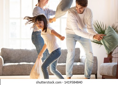 Playful Young Parents Have Fun With Little Preschooler Daughter Engaged In Pillow Fight In Living Room, Happy Family Relax Playing With Small Girl Child, Enjoy Spending Time At Home Together