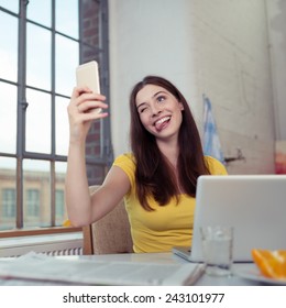 Playful young woman posing for a selfie on her mobile phone pulling a face winking and sticking out her tongue - Shutterstock ID 243101977