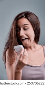 Playful young woman sticking out her tongue while reading a message on her phone, expressing a sense of fun and lightheartedness