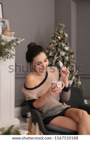 playful young woman in a transparent sweater with ginger cookies and a cup of coffee sits by the New Year tree