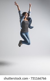 Playful young woman wearing eyeglasses jumping over grey background. Look at camera and screaming.