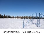 Playground equipment in a field with ground covered in snow and bright blue sky