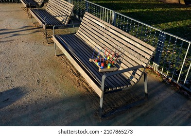 Playground Fencing Made Of Galvanized Railings With A Gate Against Dogs. Community Sandpit With Donated Colorful Puzzle Toys. Bordered By Wooden Beams Around The Sand And Logs Like Benches